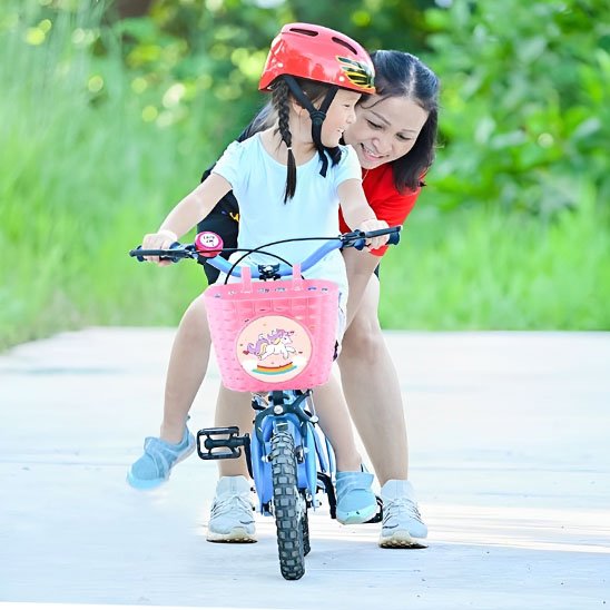 fille qui apprend a pedaler a velo avec velo panier enfant rose licorne soutenue par femme mere