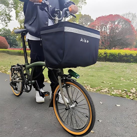 cycliste debout tenant velo de petite taille sur pave dans parc avec panier velo avant noir en nylon grande capacite sur guidon velo