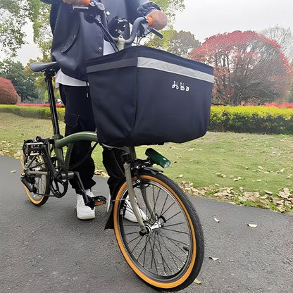 cycliste debout tenant velo de petite taille sur pave dans parc avec panier velo avant noir en nylon grande capacite sur guidon velo
