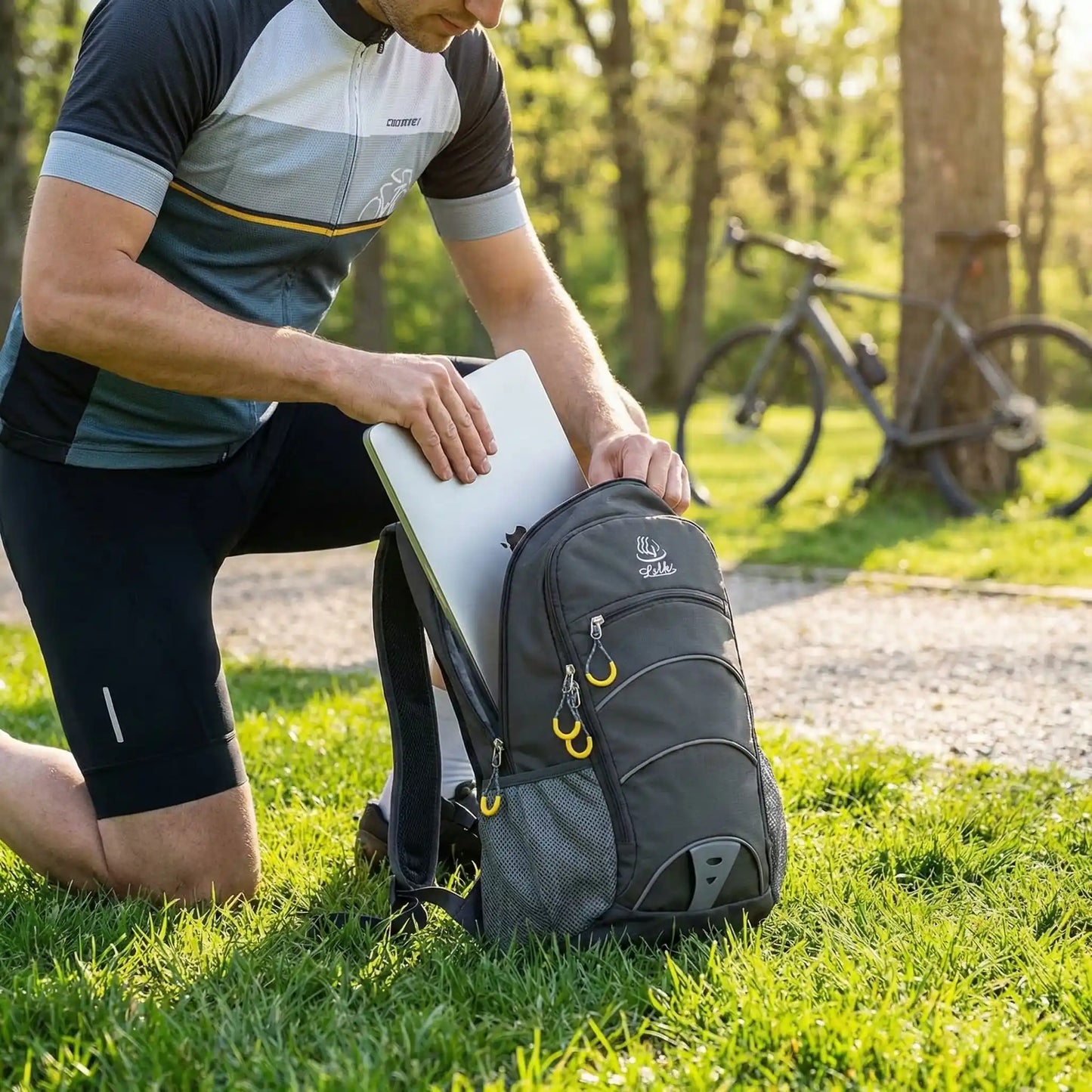 cycliste_mettant_un_laptop_dans_son_sac_de_velo_agenouille_dans_l_herbe