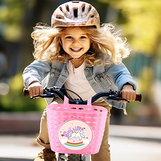 petite fille a velo avec velo panier rose autocollant licore, souriante, cheveux blonds dans le vent avec casque velo et veste de jeans.