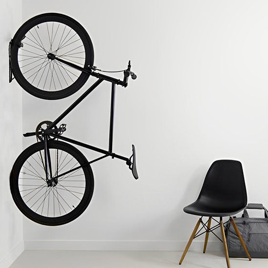 velo noir suspendu verticalement sur mur blanc par support velo propre incluant tige pour aligner et proteger surface mur et roue velo