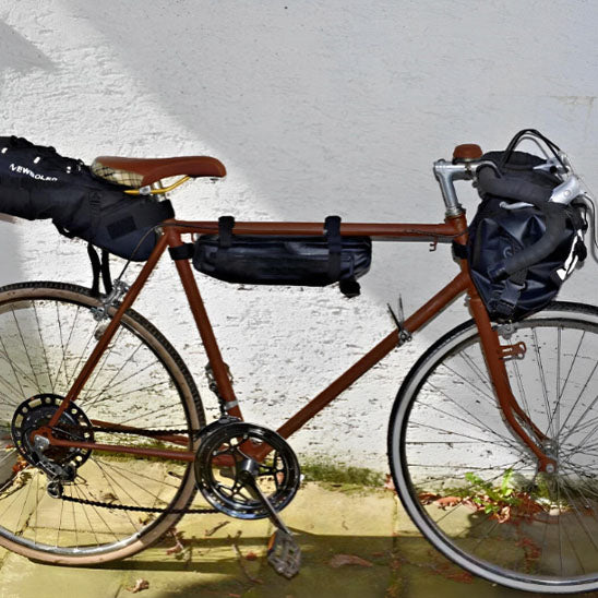 velo_vintage_brun_devant_mur_blanc_decorer_de_plusieurs_sacoche_velo_cadre_noires